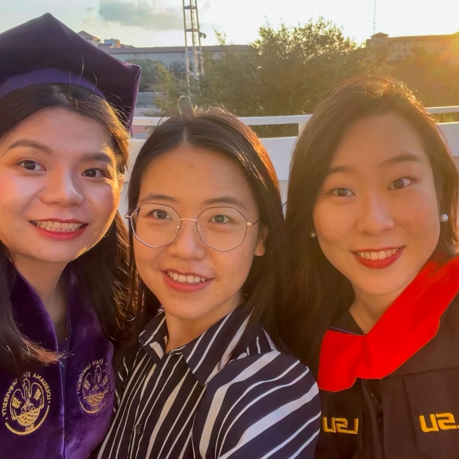 two people in graduation regalia smile with a guest